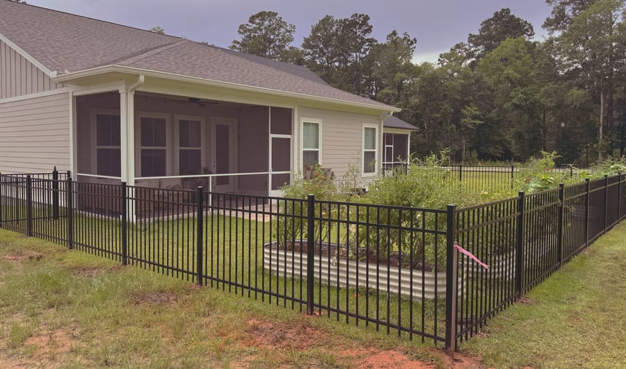A black aluminum fence enclosing a back garden, with raised planting beds inside the line.