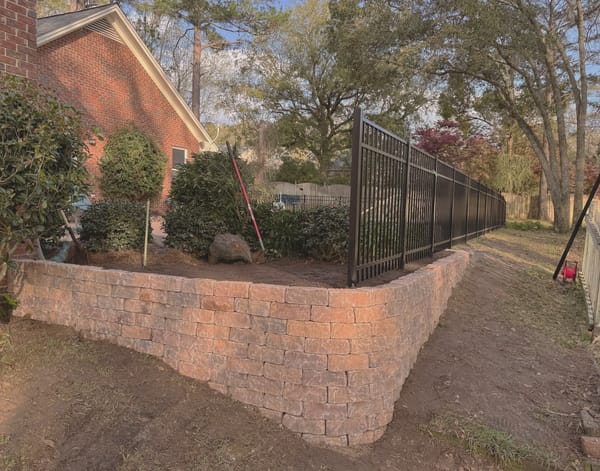 A black aluminum fence stepping down a stone retaining wall as the ground falls away.