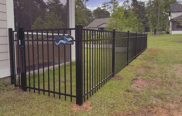 A black aluminum fence running from the corner of a house out across a lawn.