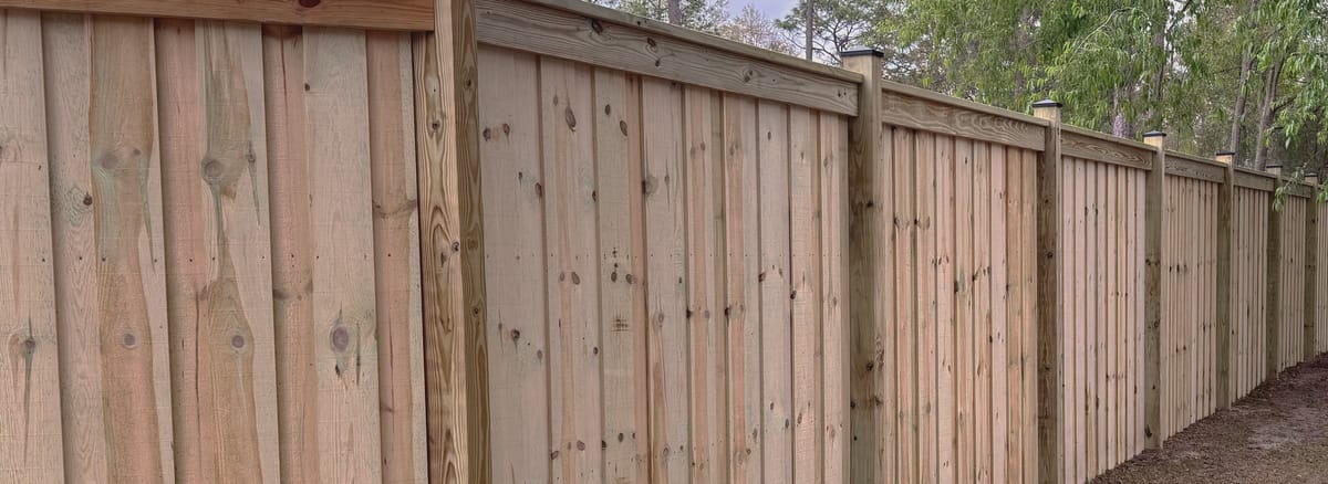 A board on board privacy fence with a capped top rail and black post caps, photographed along its length.