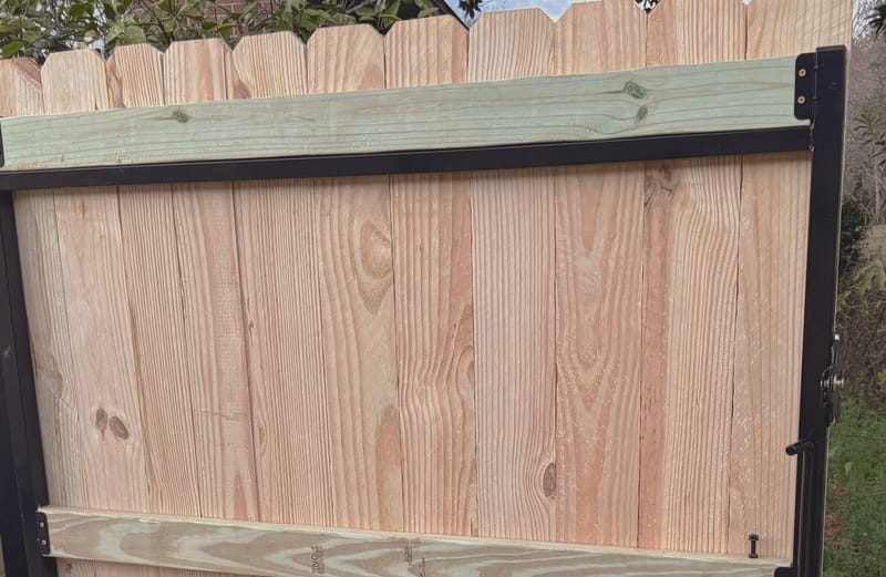 A gate leaf built on a black welded steel perimeter frame, with timber rails fixed across it and vertical boards filling the panel.