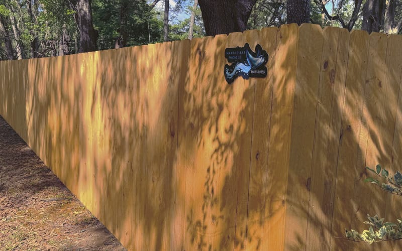 Dappled tree shadow falling across the boards of a newly built wood fence running away toward woodland.