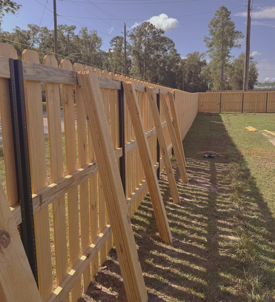 Pickets going on to a fence frame, the finished run visible beyond and the bare rails still exposed in the foreground.