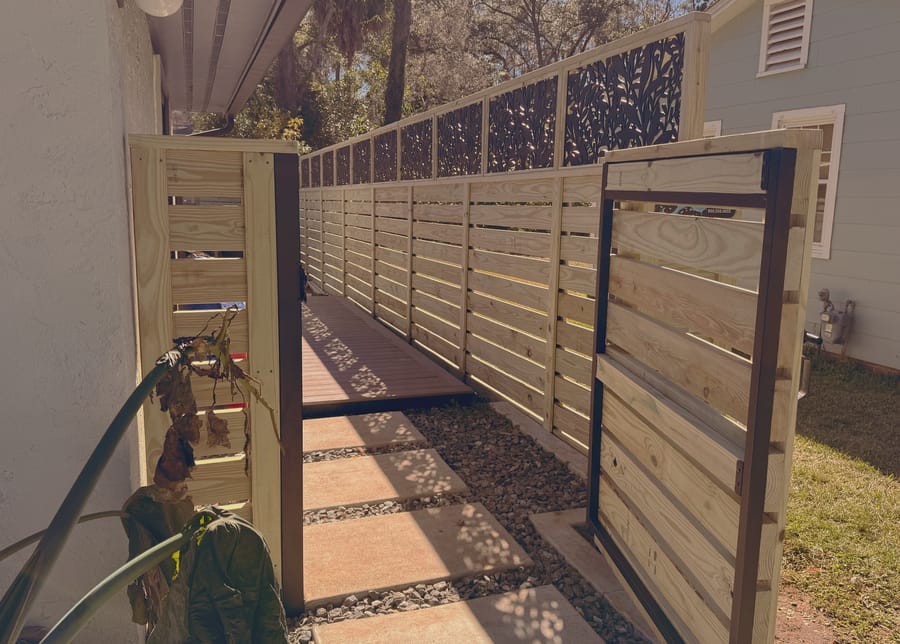 A matching horizontal slat gate in the same run, with a black frame, opening on to a stepping stone path.
