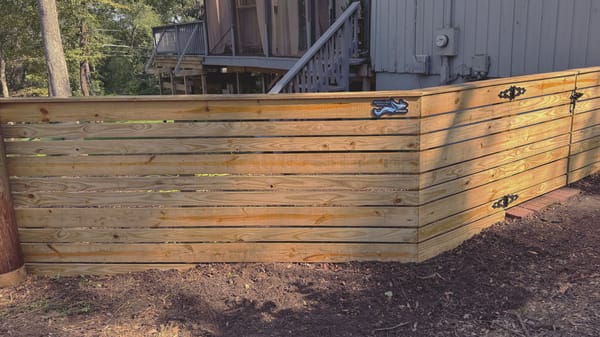 A horizontal board fence returning at a corner beside a raised house, the boards running level while the ground falls away.