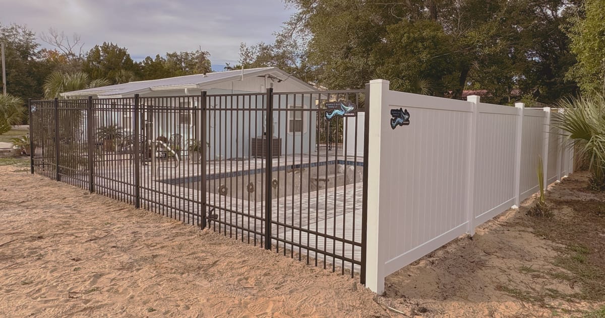 A black aluminum pool barrier enclosing a swimming pool, meeting a white privacy fence at the property line.