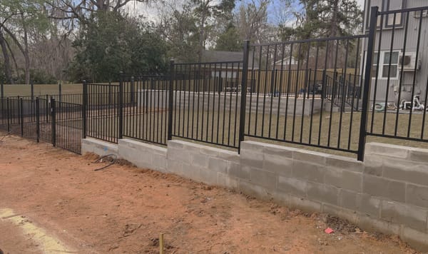 A black aluminum fence set on a block wall, running the length of a pool enclosure.