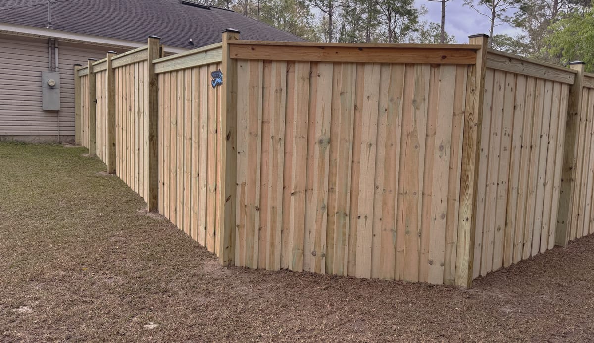 A board on board privacy fence with a capped top rail and trim, turning a corner across a large back lawn.