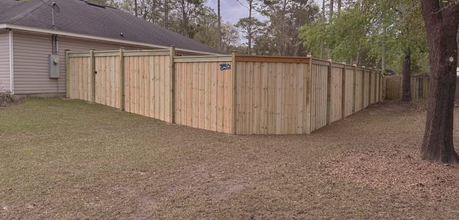 A capped board on board fence running the full width of a back garden behind a single story house.