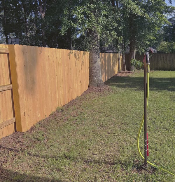 A privacy fence enclosing a lawn, running level past a large tree to a gate in the far corner.